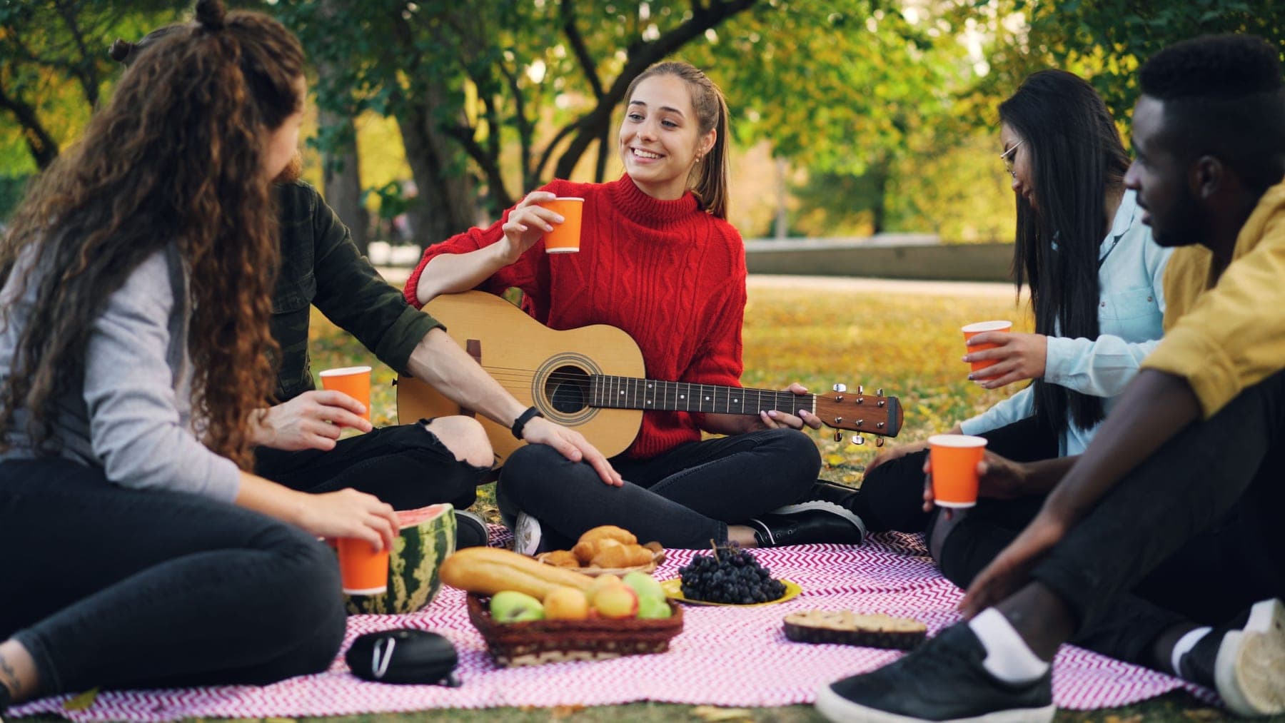 Friends sitting on a blanket in a park at sunset with music playing